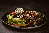Leckeres veganes Gericht mit Zucchini-Spaghetti und sautierten Pilzscheiben, bedeckt mit roten Beeren und Alfalfa-Sprossen auf dunklem Hintergrund