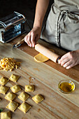 Unrecognizable person preparing raviolis and pasta at home. She is using a wooden roller
