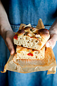 Crop person hands holding piece of fresh tomato focaccia with rosemary