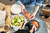 From above of crop anonymous female taking photo of delicious pastry on camera against girlfriend at kitchen table