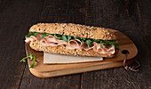 Mortadella-Sandwich von oben mit Rucola-Blättern auf dunklem Holztisch-Hintergrund