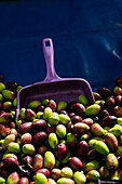 Stapel bunter, reifer Oliven mit lila Schaufel auf einem lokalen Marktstand während der Erntezeit an einem Sommertag