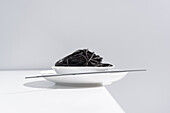 From above of ceramic bowl with delicious spaghetti with black squid ink with chopsticks on grey background