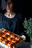 Female baker holding puff freshly baked hot cross buns on baking tray