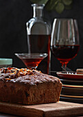 Tasty baked pound cake topped with almond flakes served on wooden cutting board on table with alcohol drink and berries