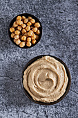 Top view of bowls of fresh hummus and chickpea placed on gray marble table in kitchen
