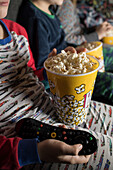 Cropped unrecognizable young siblings kids sitting comfortable on sofa with popcorn bucket while eating and watching TV