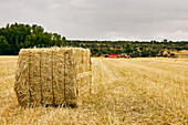 Getrocknete Heurolle und moderner Traktor auf landwirtschaftlichem Feld in bergigem Gebiet im Sommer