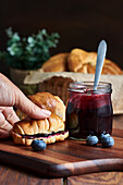 Preparation of a breakfast of croissants with blueberry jam on a wooden table