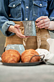 Young female blogger pouring milk from jug at table with croissants at home
