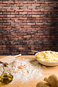Eigelb auf einem Haufen Weizenmehl in der Nähe einer Schüssel mit Kartoffelpüree und Öl bei der Zubereitung von Gnocchi-Teig auf einem Tisch in der Küche