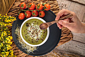 Blick von oben auf einen anonymen Koch mit einer Schüssel leckerer vegetarischer Cremesuppe mit zerstoßenen Pistazien und Gewürzen darauf