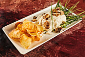 Delicious meat medallions and fried potatoes served with cheese sauce and greens on brown table in restaurant