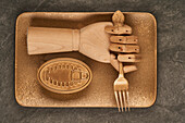 Künstliche Holzhand mit Gabel auf goldenem Tablett neben versiegelter Dose mit Konserven auf dem Tisch