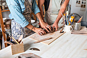 Cropped unrecognizable female and male in casual clothes and aprons smiling while creating clay plate during pottery class in workshop