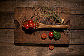 Top view composition of fresh ripe red cherry tomatoes with aromatic basil leaf and bunch of thyme on wooden cutting board with spoon