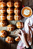 From above hand with appetizing freshly baked sourdough hot cross buns and mug of coffee on wooden table