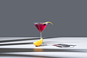 Composition of glass filled with red fruit cocktail near orange slides and zest placed on concrete table against grey background