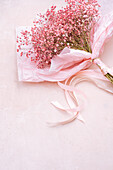 From above bouquet of small tender Gypsophila flowers with green stalks in paper wrapping placed on pink background in light room