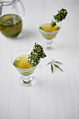 Small glasses with medical marijuana tea and green herbs placed on white surface near glass jar