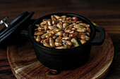 High angle of heap of cereal grain in black saucepan with lid placed on wooden board on table in kitchen