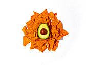 Top view of half of fresh avocado placed on pile of crunchy tortilla chips on white background