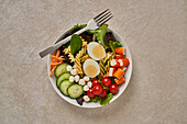 Gesunder Salat mit verschiedenen Gemüsesorten und Nudeln mit gekochten Eiern und Grünzeug in einer Schüssel mit Gabel auf einem Steintisch serviert