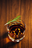 Ein Glas Whiskey mit Rosmarin auf einem Holztisch