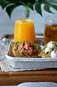 Gläser mit Saft und Kräutertee, serviert auf einem Holztisch mit verschiedenen gesunden Avocado-Toasts mit Käse und Lachs während des Frühstücks in einem Straßencafé