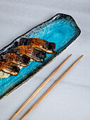 Grilled smoked eel nigiri over blue ceramic plate
