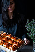 Female baker holding puff freshly baked hot cross buns on baking tray