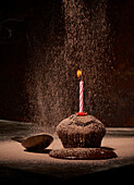 Puderzucker bestreut auf leckeren süßen Geburtstagsmuffin mit Puderzucker und gelöschter Kerze auf Tisch mit verschütteter Schokolade und Löffel auf dunklem Hintergrund serviert