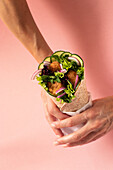 Cropped unrecognizable person hands holding vegan falafel wrap on colorful pink background