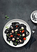 Von oben schwarzer Tinte Spaghetti mit Lachs in Keramikteller auf dunklem Hintergrund