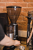 Crop anonymous barista preparing fresh ground coffee in portafilter of professional grinder in cafe