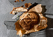 Top view of delicious freshly baked sourdough bread loaf with sliced piece and knife placed on baking paper on gray background