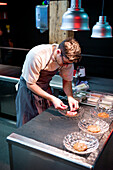 Young serious chef man in cooking apron serving meal in dishes on restaurant kitchen