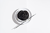 Blick von oben auf eine Keramikschale mit leckeren Spaghetti mit schwarzer Tintenfischtinte und Stäbchen auf weißem Hintergrund