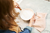 Content young female in apron whipping sweet cream while cooking at table in light house