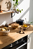 Verschiedene Zutaten und Utensilien auf einem Holztisch während des Kochvorgangs in einer Küche mit weißen Wänden und minimalistischem Interieur im natürlichen, umweltfreundlichen Stil