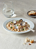 Appetizing traditional spanish stewed white fabes beans with mollusks in plate with fresh parsley leaves on tablecloth
