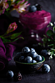 Closeup of pile of ripe blueberries in bowl served on black table with purple cloth