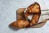 Freshly baked croissants served on wooden cutting board with napkin on table for breakfast