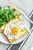 From above toast with eggs and cheese and rocket lettuce served on plate on table background