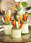Composition of tasty zucchini rolls with stuff of avocado cream and straws of colorful bell pepper placed on metallic tray