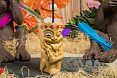 Polynesian tiki cup of cold alcohol beverage decorated with straw and green leaves placed against colorful leaves and dry grass