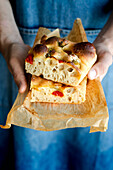 Crop person hands holding piece of fresh tomato focaccia with rosemary