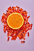 Komposition aus reifen, geschnittenen Orangen auf rosa Fläche neben verstreuten Pillen in einem hellen Studio