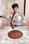 Hispanic man in uniform and glasses pouring liquid chocolate from bowl on marble board during work in confectionery