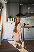 Side view of millennial female looking down at table with glass of milk and tasty oat biscuits in kitchen